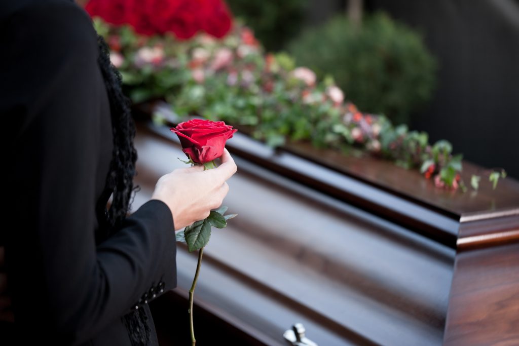 woman placing rose on christian casket funeral