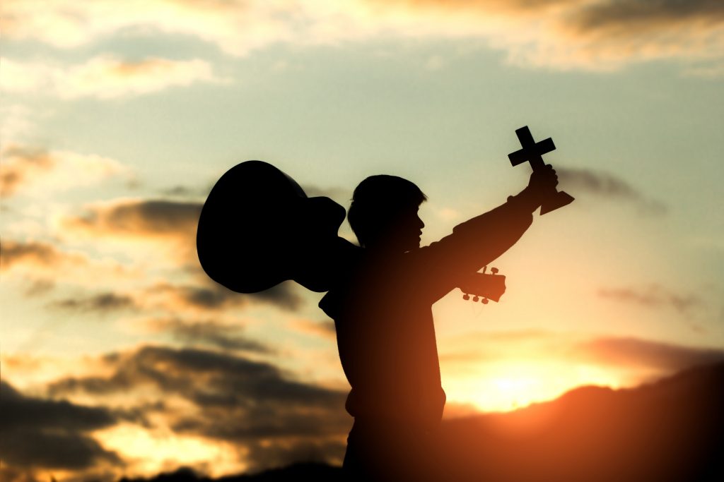 a man carrying a guitar and a christian cross